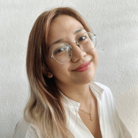 A picture of Bianca Aguilar: a bespectacled Filipina with brown hair and blonde highlights. She is wearing a necklace with her blouse, and smiling at the camera.